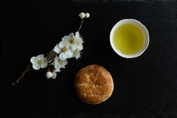 Kamayaki Manju, Traditional Japanese sweets, Ume (apricot) flower branch and Japanese green tea in a beauty minimalist aesthetic arrangement on black granite board background. Japan.