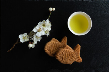 Taiyaki, Traditional Japanese sweets, Ume (apricot) flower branch and Japanese green tea in a beauty minimalist aesthetic arrangement on black granite board background. Japan.