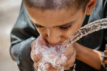 A thirsty Pakistani boy drinking water from a water supply tap on a hot day