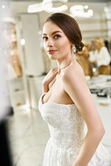 Naklejka premium A young brunette bride in a white wedding dress strikes a pose for a picture in a wedding salon.