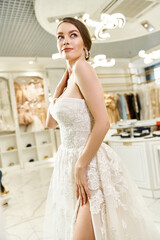 A young brunette bride poses in a white dress, exuding elegance and beauty during a photoshoot in a wedding salon.