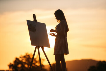 Silhouette of blonde girl paints a painting on the canvas.Palette with paints and spatula, summer...
