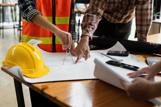 Architects Collaborating on Construction Project with Blueprints and Safety Gear in Modern Office Setting