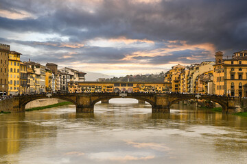 Fototapeta premium Dramatic sunset on the Arno River with the Ponte Santa Trinita and the Ponte Vecchio in the background, that connect the two sides of the historic centre of Florence, Tuscany, Italy