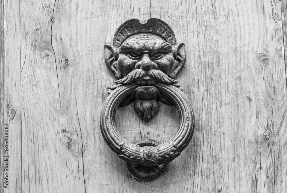 Wall mural black and white photo. close-up of an old wrought iron knocker depicting the head of a satyr or demo