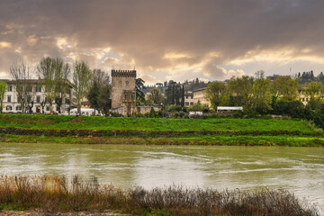 Fototapeta premium The Arno river banks with the Torrino of Santa Rosa, a tower that was part of the ancient, defensive city walls (13-14th centuries), with a dramatic storm sky, Florence, Tuscany, Italy