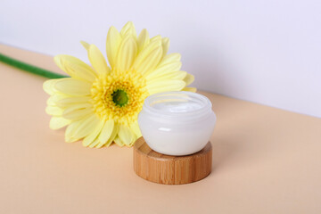 Cosmetic cream jar and yellow gerbera flowers on neutral background. Closeup