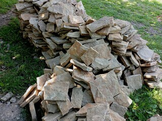 A mountain of yellow decorative sandstone in crushed slabs is piled up for decorating concrete walls. Construction decorative material is dumped on the grass at the construction site.
