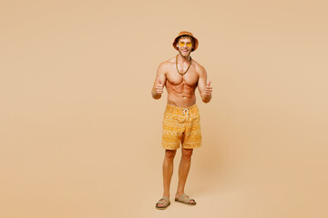 Full body young smiling man wear yellow shorts swimsuit hat relax rest near hotel pool showing thumb up like gesture isolated on plain beige background. Summer hot vacation sea rest sun tan concept.