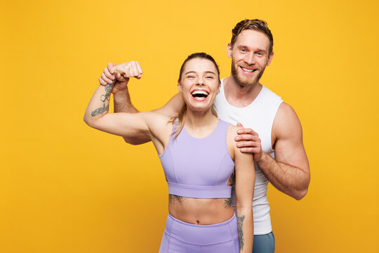 Young cool strong fitness trainer instructor sporty two man woman wear blue clothes spend time in home gym showing biceps muscles on hand isolated on plain yellow background Workout sport fit concept
