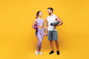 Full body young strong fitness trainer sporty two man woman wearing blue clothes spend time in home gym hold yoga mat look to each other isolated on plain yellow background. Workout sport fit concept.