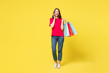 Full body young woman wear pink casual clothes hold package bags after shopping sharing hot news about sales scream, hand near mouth isolated on plain yellow background. Black Friday sale buy concept.