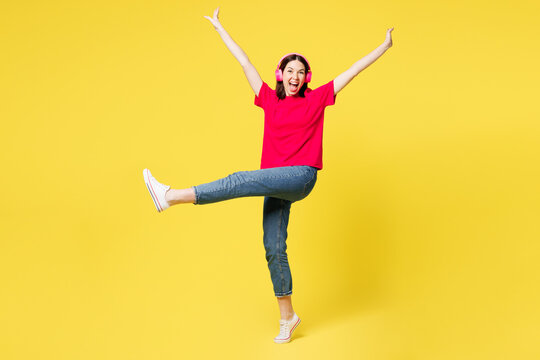 Full body young happy woman she wear pink t-shirt casual clothes listen to music in headphones dace raise up legs hands isolated on plain yellow orange background studio portrait. Lifestyle concept.