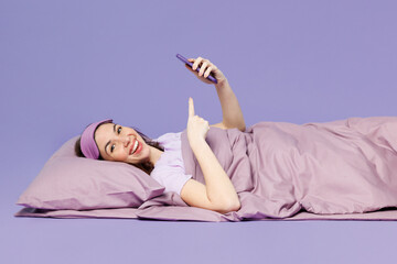 Side view young calm woman in pyjamas jam sleep eye mask rest relax at home lay down on bed hold...
