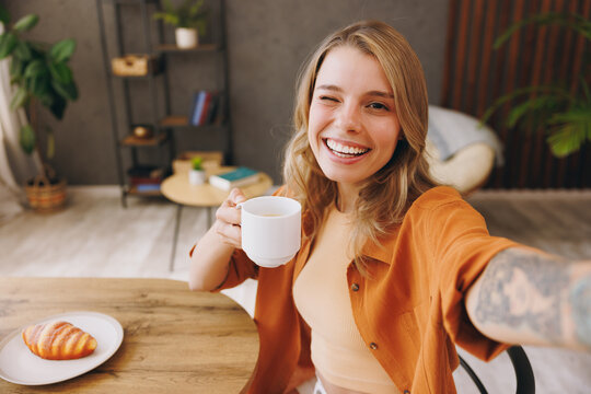 Close up young happy woman wear orange shirt do mobile cell phone selfie shot sits alone at table in coffee shop cafe relax rest at restaurant in free time indoors. Freelance office business concept.