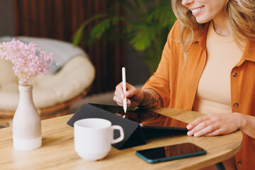 Cropped young woman wears orange shirt use digital tablet pc computer write draw stylus pc pen sits...