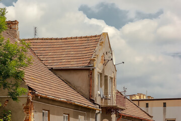 Stary ceglany dom z dachem pokrytym dachówką ceramiczną. Zabytkowy dom (lekko uszkodzony) na tle lekko zachmurzonego czerwcowego nieba.