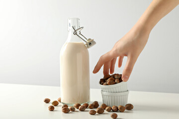 Bottle with milk, hand and bowls with nuts on white background