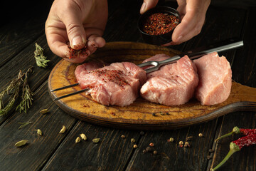 Chef cooks meat steaks with aromatic spices on the kitchen table in the restaurant. Concept of cooking barbecue from juicy beef. Asian cuisine