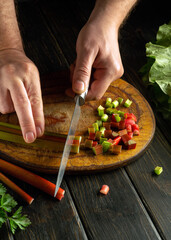 A chef uses a knife to cut rhubarb on a wooden cutting board to prepare a vitamin-rich salad.