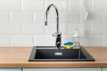 A clean empty black kitchen sink in a kitchen with a chrome faucet, wooden countertop, and white...
