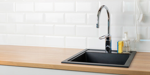 A clean empty black kitchen sink in a kitchen with a chrome faucet, wooden countertop, and white...