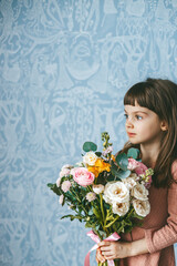 A cute little girl holding a bouquet of flowers, featuring roses, eucalyptus, ranunculus and other species