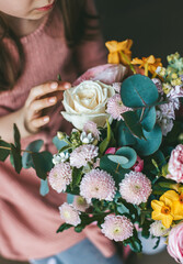 A little girl touching a vibrant bouquet of flowers, showcasing pink, white, and yellow roses among other floral species