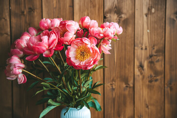 Pink peonies in vase, positioned in front of a wooden backdrop