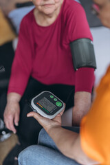 An elderly woman sits on a bed and has her blood pressure taken by a female volunteer