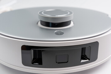 A white and silver device with a black button on the front. Robot vacuum cleaner on a white background.