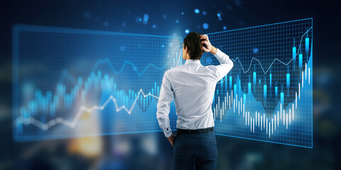 A businessman analyzing financial graphs floating in the air on a blue high-tech background, concept of analytics