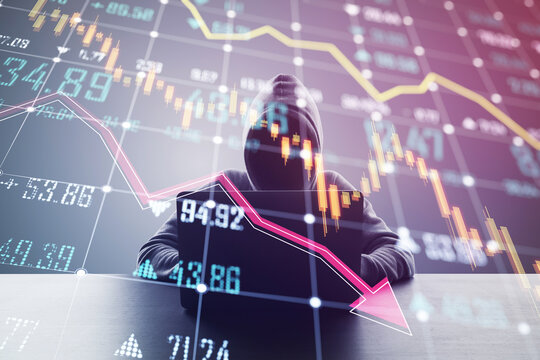 A person in a hoodie using a laptop with a double exposure of declining financial graphs, concept of economic downturn