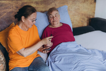 A female nurse checks an elderly man's blood sugar levels while sitting next to him and poking his...