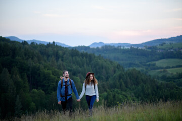 Travellers couple hiking on trail in nature with backpacks, during sunset. Young tourist spending...