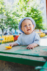 Fototapeta premium A little baby boy, 11 months old, in a t-shirt and a panama on his head, plays with sand on a summer day. A child is playing on the street.