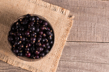 Black currant in a bowl on wooden background. Organic berries. 
