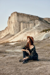 Woman wearing hat sits in front of mountain, admiring scenic view on sunny day