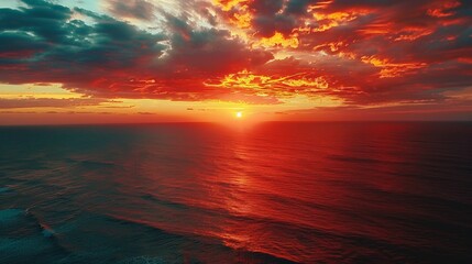 Fototapeta premium Aerial shot of a vibrant sunset over a vast ocean, with dramatic clouds ablaze with color