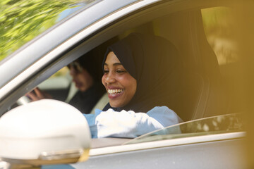 Two Muslim women wearing hijab converse on a smartphone while traveling together in a car through...