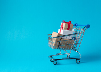 Gift boxes in shopping cart on blue background. Minimal sale con