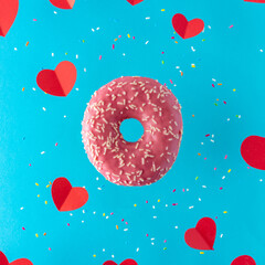 Pink donut with red paper hearts on a bright blue background. Minimal love concept.