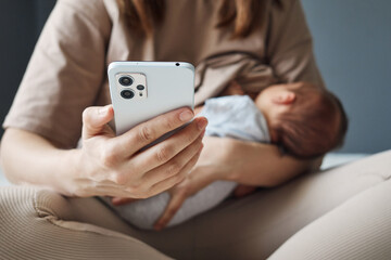 Unrecognizable unknown woman breastfeeding baby and using social media to stay in touch while...