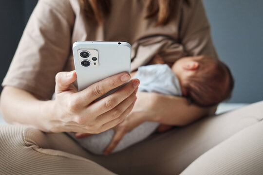 Unrecognizable unknown woman breastfeeding baby and using social media to stay in touch while maternity leave woman nursing child and holding smartphone