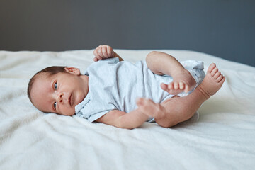 Infancy, healthcare and pediatrics, growth. Close up view of cutie newborn wearing bodysuit lying alone on bed adorable baby resting on bedsheets moving playing