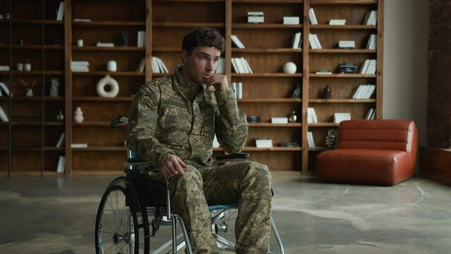 Pensive stressed sad Caucasian male officer camouflage uniform disabled man military army soldier guy veteran wheelchair touching hold head suffering pain post traumatic stress war disability indoors