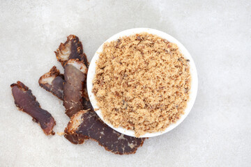 Flat lay of powdered biltong with sliced biltong on the side with copy space on light grey surface