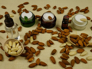 Jars of cosmetic creams, bottles with tonic based on the almonds oils placed on the white burlap...