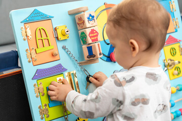 A toddler uses a key for a small lock while playing with a busy board