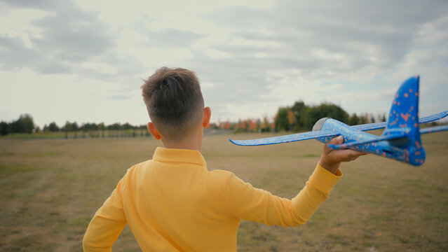 Back view adorable kid Caucasian little boy son schoolboy jog teen play with toy plane outdoors beautiful nature park field. Child playing run throw launching flying airplane flight dream become pilot